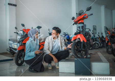 young man and veiled saleswoman squatting near a motorcycle 119088936