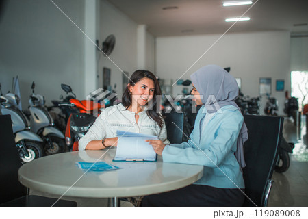 young woman and veiled saleswoman chat while reading the approval letter young woman and veiled saleswoman chat while reading the approval letter 119089008