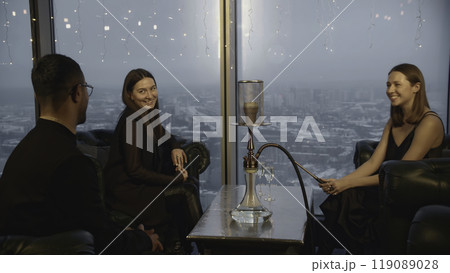 Man meets women in hookah bar. Media. Man sits down with young women to meet in restaurant. Company of elegant adults in hookah restaurant 119089028