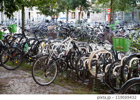 A crowded urban bicycle parking area showcasing eco-friendly transportation in a city. Represents sustainability, urban biking culture, and minimalist lifestyle trends with greenery in the background. A crowded urban bicycle parking area showcasing eco-friendly transportation in a city. Represents sustainability, urban biking culture, and minimalist lifestyle trends with greenery in the background. 119089432