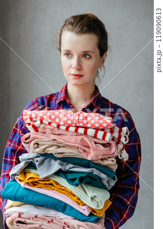 happy young European woman holds stack of folded clothes for hygienic washing at home.  119090613
