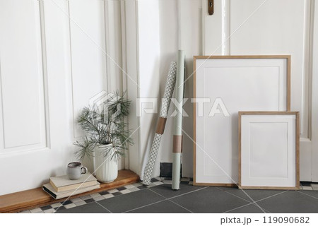Festive Christmas indoor decor. Set of blank vertical wooden picture frames mockups, grey tiled floor. Pine tree branches in vase gift wrapping papers. White hall background. Empty artistic templates. 119090682