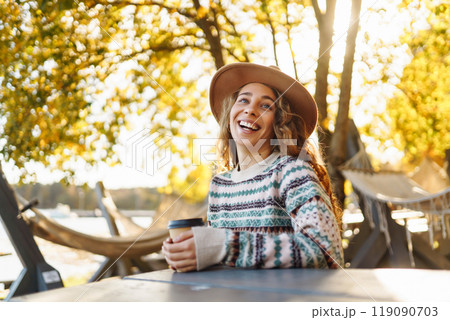 Fall concept woman drinking coffee on bench against backdrop of lake. Enjoying, solitude with nature 119090703