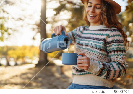 Woman holds thermos and drinks tea in sunny autumn forest. Vacation, travel, lifestyle concept. Woman holds thermos and drinks tea in sunny autumn forest. Vacation, travel, lifestyle concept. 119090706