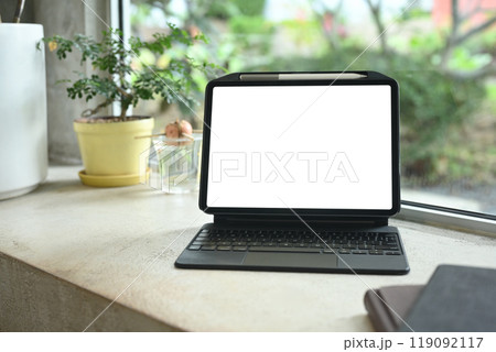 Digital tablet with blank screen on a table next to a potted plant and notebooks Digital tablet with blank screen on a table next to a potted plant and notebooks 119092117