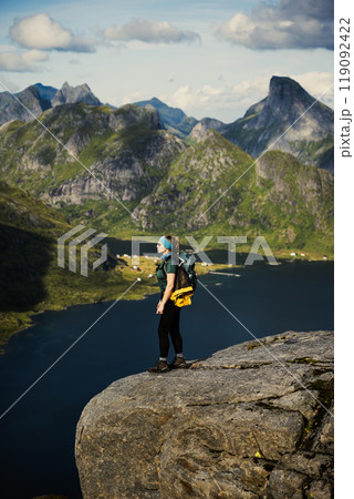 A hiker on a cliff in the majestic Lofoten fjord landscape with mountains and sky on background 119092422
