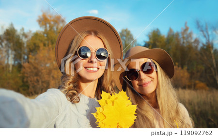 Happy young two women friends taking selfie with phone, autumn yellow leaves, girlfriends in park Happy young two women friends taking selfie with phone, autumn yellow leaves, girlfriends in park 119092762
