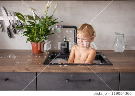 Cute happy baby girl with playing with water and foam in a kitchen sink at home Cute happy baby girl with playing with water and foam in a kitchen sink at home 119094360