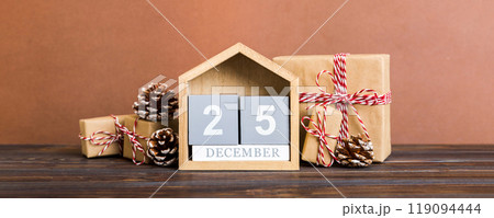 25 december. Christmas composition on colored background with a wooden calendar, with a gift box, toys, bauble copy space 25 december. Christmas composition on colored background with a wooden calendar, with a gift box, toys, bauble copy space 119094444