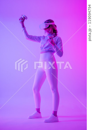Woman immersed in virtual reality with headset and controllers in neon lights Woman immersed in virtual reality with headset and controllers in neon lights 119094794