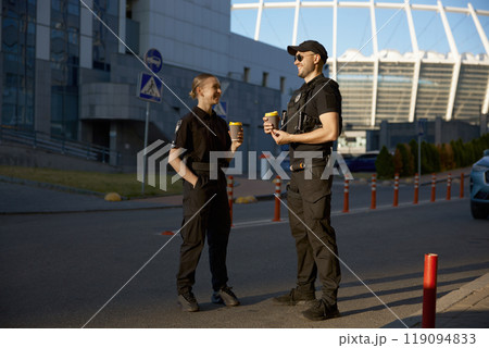 Cheerful patrol officers talking together drinking coffee having work break Cheerful patrol officers talking together drinking coffee having work break 119094833