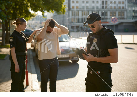 Policeman filling out offense form, while policewoman calming down upset citizen Policeman filling out offense form, while policewoman calming down upset citizen 119094845