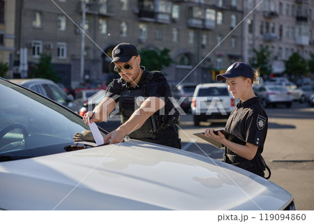 Police patrolman and patrolwoman putting fine for car parking in wrong place Police patrolman and patrolwoman putting fine for car parking in wrong place 119094860