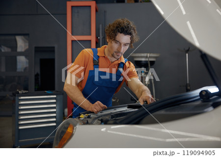 Male mechanic looking under car hood checking engine operation work 119094905