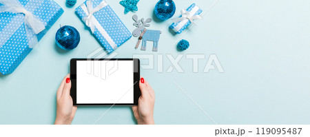 Top view of woman holding tablet in her hands on blue background made of Christmas decorations. New Year holiday concept. Mockup Top view of woman holding tablet in her hands on blue background made of Christmas decorations. New Year holiday concept. Mockup 119095487