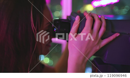 Woman on a rooftop at night, using binoculars to observe the vibrant city lights below, filled with wonder and excitement Woman on a rooftop at night, using binoculars to observe the vibrant city lights below, filled with wonder and excitement 119096946