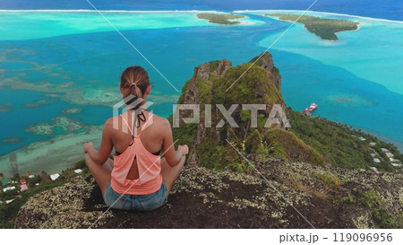 Young woman is practicing yoga and enjoying a moment of peace while admiring the scenic view of maupiti island lagoon in french polynesia 119096956