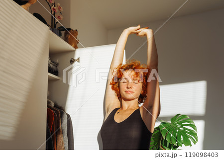 portrait of young red-haired woman choosing clothes in closet at home 119098403