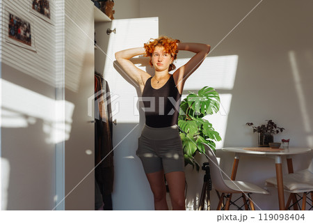 portrait of young red-haired woman choosing clothes in closet at home 119098404