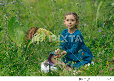 A young girl is sitting peacefully and contentedly in a lush green field, surrounded by vibrant wildflowers A young girl is sitting peacefully and contentedly in a lush green field, surrounded by vibrant wildflowers 119098992