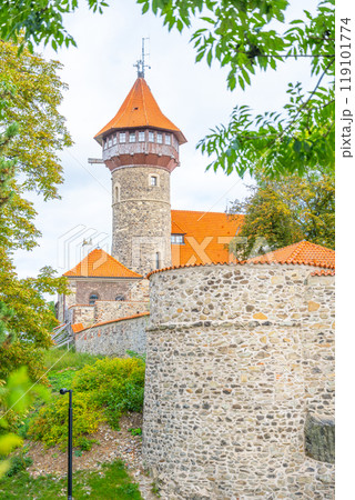 The striking lookout tower of Hnevin Castle rises above mossy walls, offering a glimpse into the rich history of Most, Czechia. The orange rooftops contrast beautifully with the stone structure. 119101774
