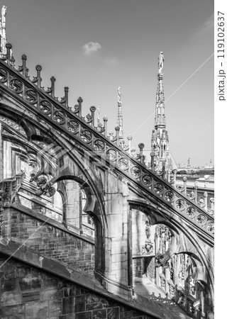 The stunning ornamental rooftop of the Duomo in Milan showcases intricate stone carvings and sculptures under a clear sky, reflecting the architectural beauty of this historic cathedral. 119102637