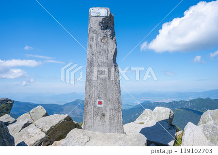 The summit of Dumbier stands proudly with a stone marker against a backdrop of clear blue sky and distant mountains, showcasing the breathtaking landscape of the Low Tatras. 119102703