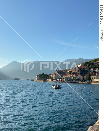 Coastal town basks in the soft glow of evening light, nestled against a backdrop of majestic mountains and tranquil waters. Harmony of architecture and nature, inviting exploration and relaxation 119103491