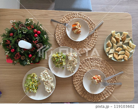 Festive dining table set with an assortment of homemade dishes, complemented by a decorative holiday wreath centerpiece. Warmth and joy of gathering for a shared meal during holiday season Festive dining table set with an assortment of homemade dishes, complemented by a decorative holiday wreath centerpiece. Warmth and joy of gathering for a shared meal during holiday season 119103602
