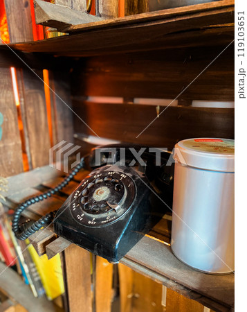 Vintage rotary phone sits on a rustic wooden shelf, accompanied by a simple metal tin. this image captures a sense of nostalgia and timeless charm, evoking memories of past eras Vintage rotary phone sits on a rustic wooden shelf, accompanied by a simple metal tin. this image captures a sense of nostalgia and timeless charm, evoking memories of past eras 119103651