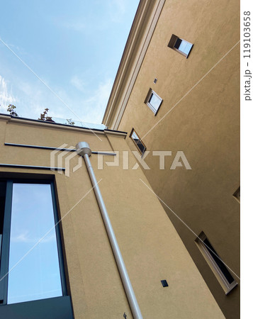 Looking up at the intersection of two modern beige buildings against a bright blue sky. Minimalist urban scene, highlighting the contrast between architecture and open sky 119103658