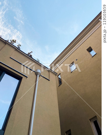 Looking up at the intersection of two modern beige buildings against a bright blue sky. Minimalist urban scene, highlighting the contrast between architecture and open sky 119103659