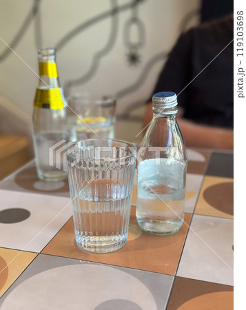 Glass of water alongside a bottle on a patterned tile table. Depicting everyday hydration and minimalistic lifestyle themes. Glass of water alongside a bottle on a patterned tile table. Depicting everyday hydration and minimalistic lifestyle themes. 119103698