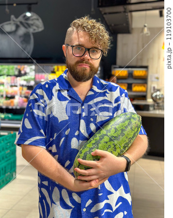 Millennial man holding a watermelon in a grocery store. Moment of everyday life with a vibrant display of produce and personal style 119103700