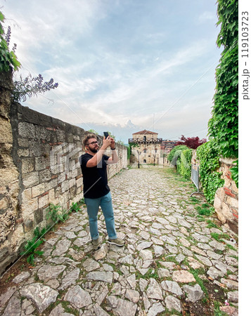 A man takes a photo while standing at a viewpoint in fortress. A tourist with a smartphone camera A man takes a photo while standing at a viewpoint in fortress. A tourist with a smartphone camera 119103723