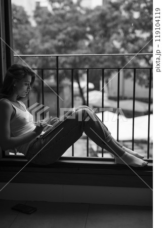 A contemplative woman is engaged in writing by a window, captured beautifully in black and white 119104119