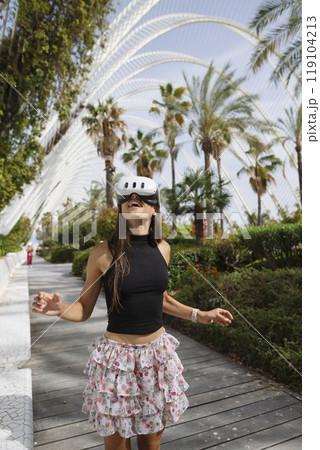 A young woman skating joyfully in a stylish summer outfit among palm trees on a sunny day A young woman skating joyfully in a stylish summer outfit among palm trees on a sunny day 119104213