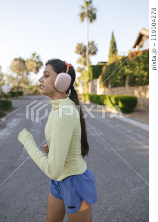 A Young Woman Jogging Outdoors while Wearing Headphones, Enjoying the Fresh Air and Music 119104278