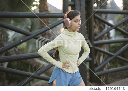 A young woman jogs outdoors with headphones, embodying a vibrant, active lifestyle 119104348