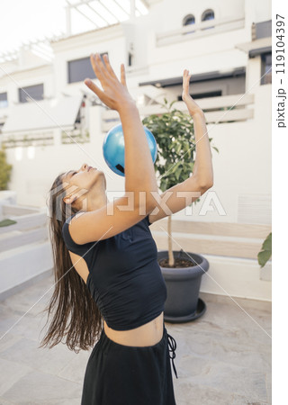 A Dynamic Young Woman Gracefully Balancing a Blue Ball in a Beautiful Outdoor Setting 119104397