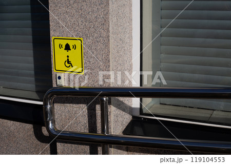 Hand rails to assist person in wheelchair next to handicap sign on wall and call button to assist person with disability, modern entrance to building with convenient ramp for people with disabilities 119104553