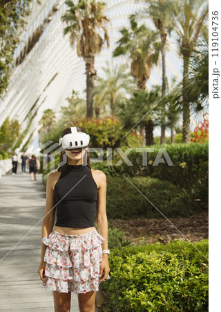 A young woman in VR gear explores a beautiful tropical landscape, enjoying her adventure A young woman in VR gear explores a beautiful tropical landscape, enjoying her adventure 119104736