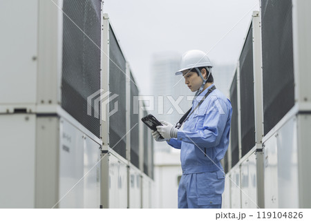 ビルメンテナンス イメージ ビル屋上に設置された空調の室外機を点検する作業服姿の男性の横顔 ビルメンテナンス イメージ ビル屋上に設置された空調の室外機を点検する作業服姿の男性の横顔 119104826