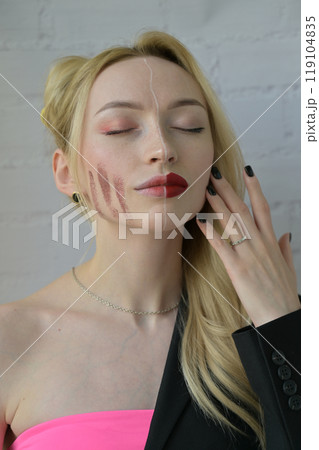 Close-up portrait of a blonde girl with different make-up on half of her face with hand near face on white background Close-up portrait of a blonde girl with different make-up on half of her face with hand near face on white background 119104835