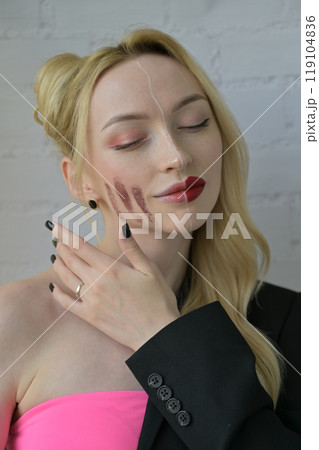 Close-up portrait of a blonde smiling girl with different make-up on half of her face with hand near face on white background Close-up portrait of a blonde smiling girl with different make-up on half of her face with hand near face on white background 119104836