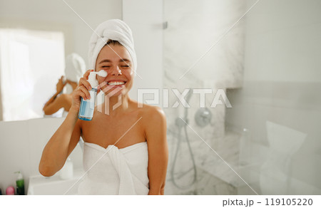 A Joyful Woman Happily Applying Skincare Products in a Beautiful, Modern Bathroom Space 119105220