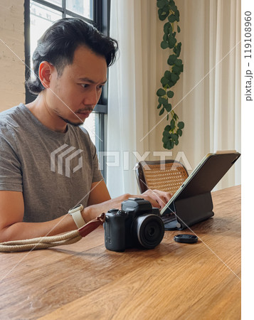 Serious photographer man working with his computer tablet at the wooden desk. Serious photographer man working with his computer tablet at the wooden desk. 119108960