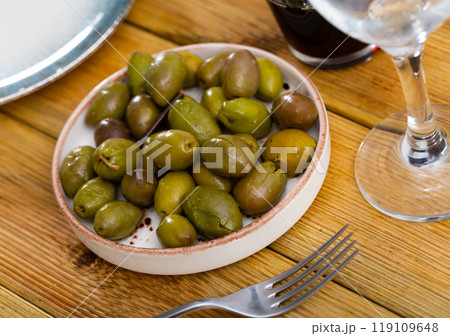 Serving of fresh pitted olives on plate with a glass of red wine 119109648