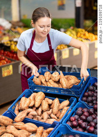 Smiling saleswoman lying out boxes of sweet potatoes in farmers market 119109718