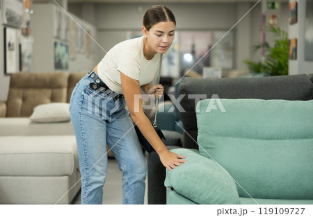 Interested young girl choosing new sofa in furniture salon 119109727